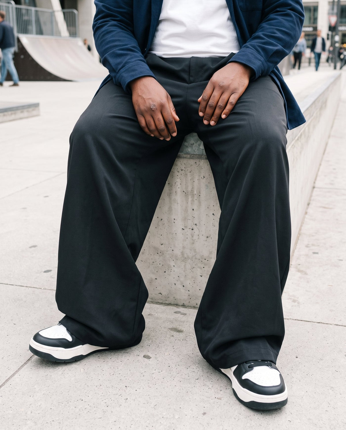 The Envoy trousers in black seated on a concrete ledge at a skate park