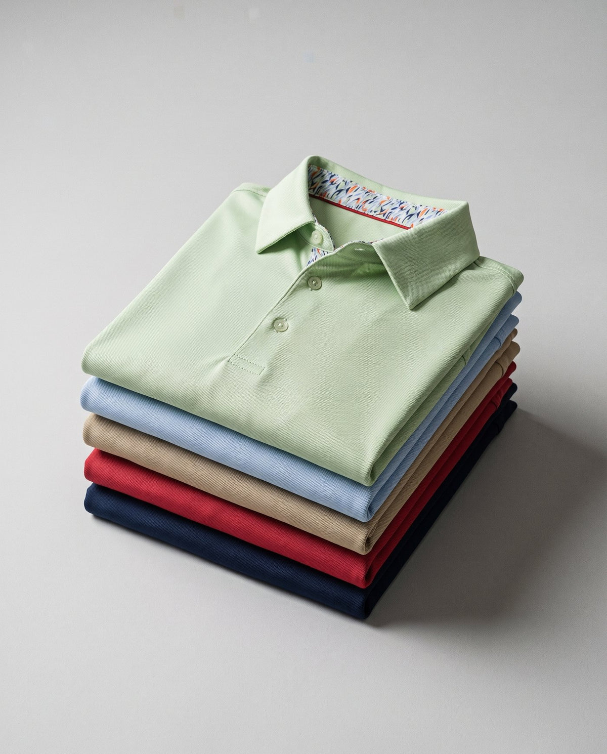 Meridian golf polos folded in a stack showing five colourways