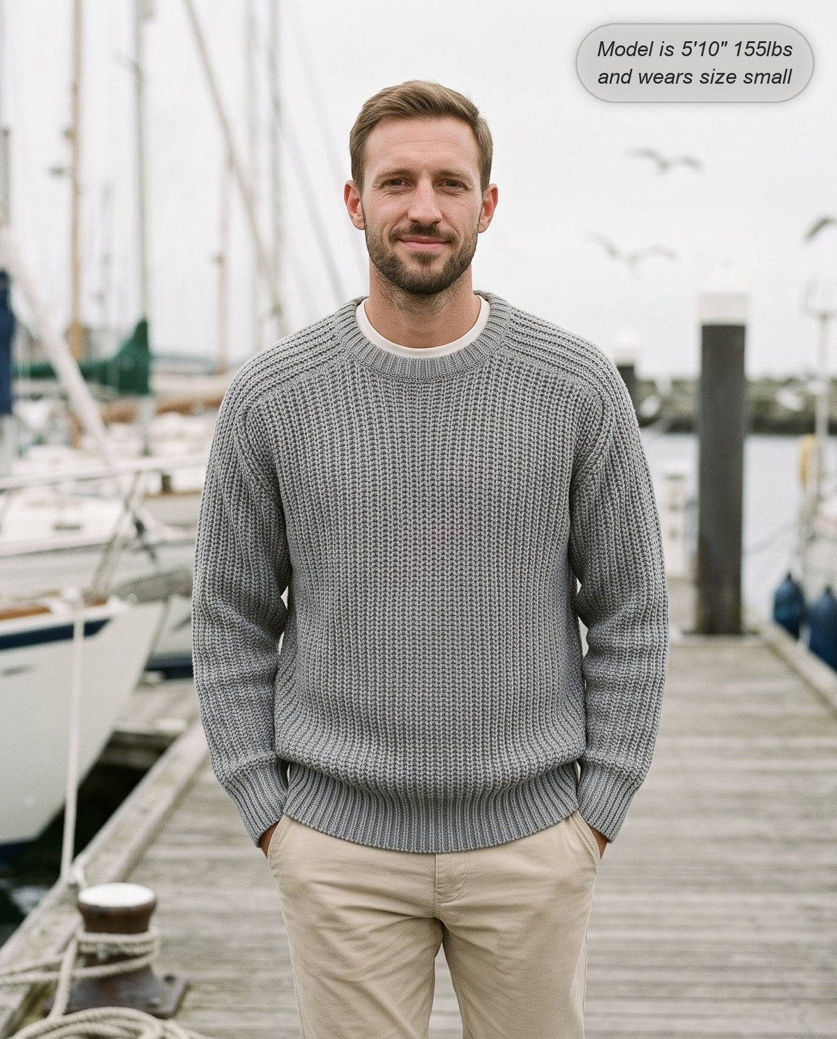 Man wearing the Admiral relaxed ribbed knit sweater in gray on a harbour boardwalk