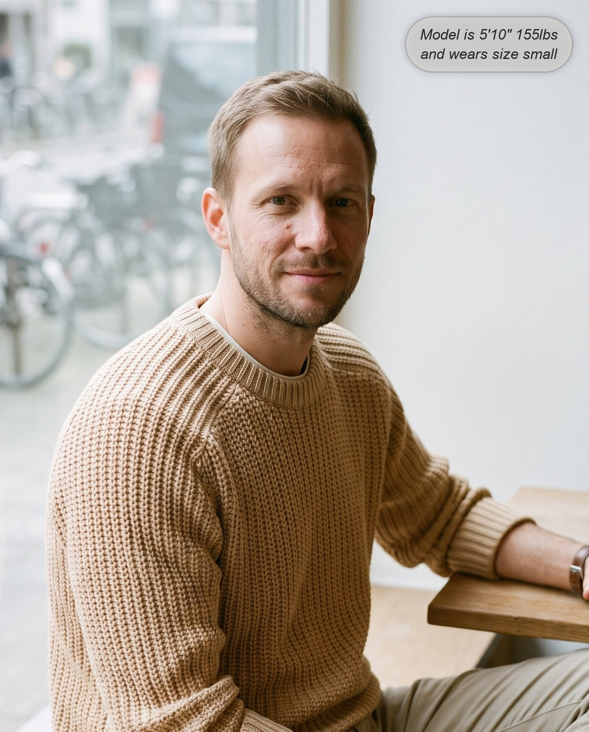 Man wearing the Admiral relaxed ribbed knit sweater in beige at a cafe window