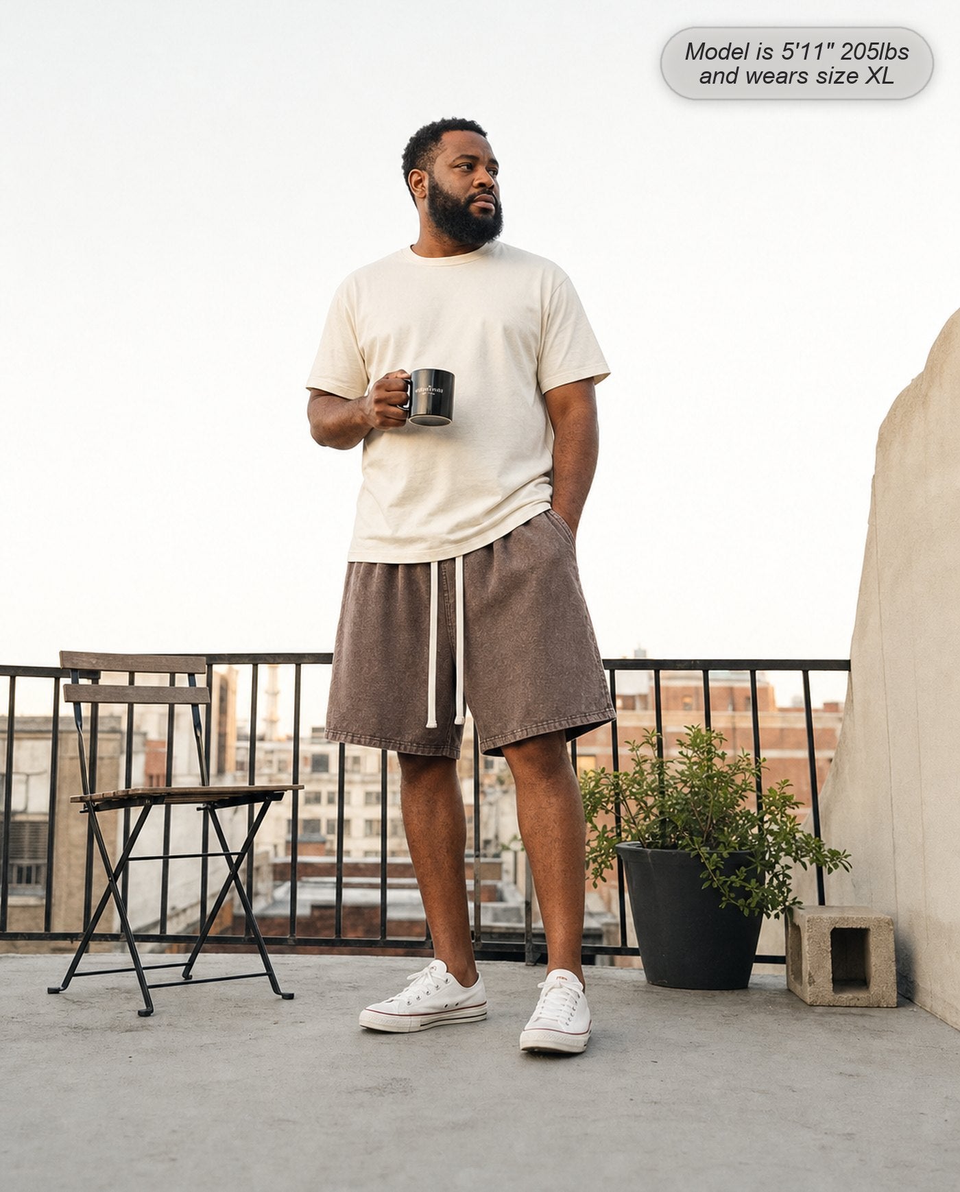 Man wearing Colossus shorts in coffee brown on an apartment balcony