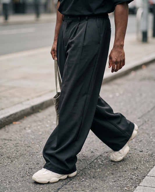 Close view of the wide leg and stacked hem of the Envoy trousers in black