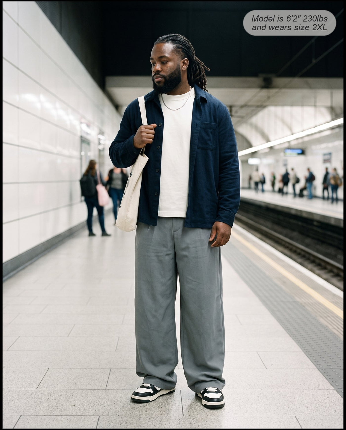 Man wearing the Envoy pleated wide leg trousers in charcoal on a subway platform