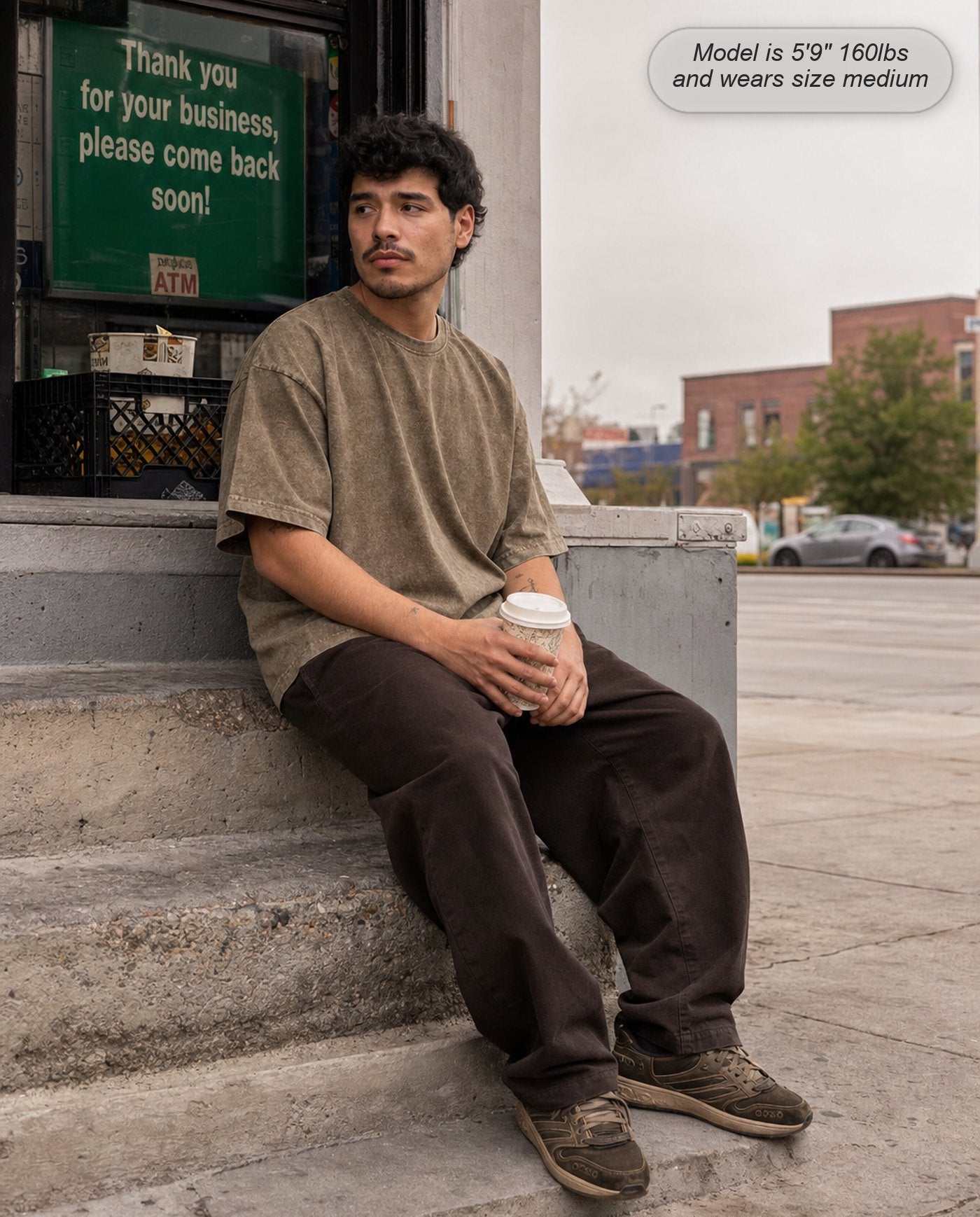 Man in an Olive Brown Legion oversized acid wash tee sitting on a stoop