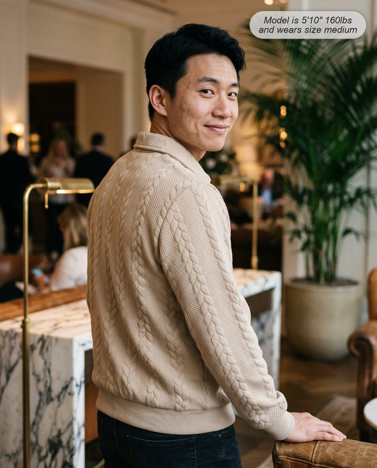 Man wearing the Regent quarter zip knit in sand in a hotel lobby